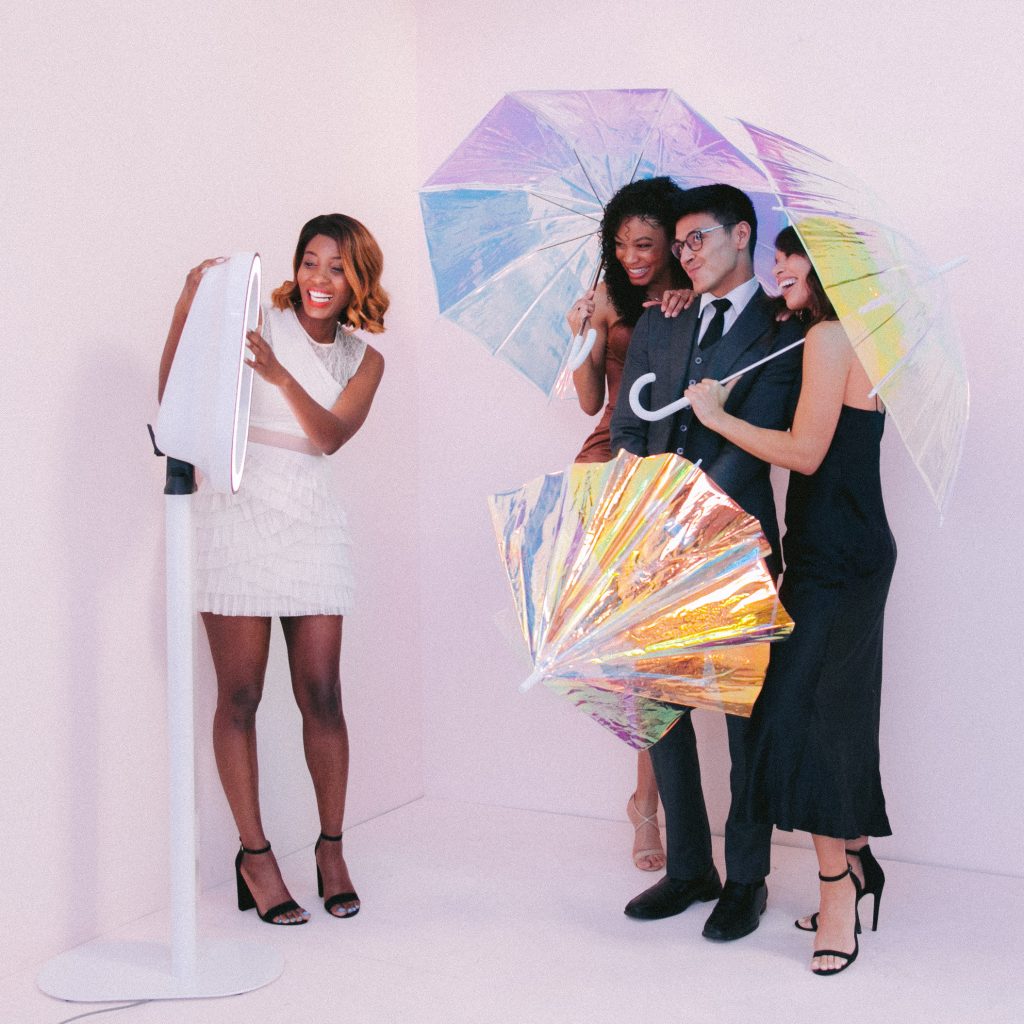 A woman using a photo booth to take photos of a man and two other women posing with colorful umbrellas