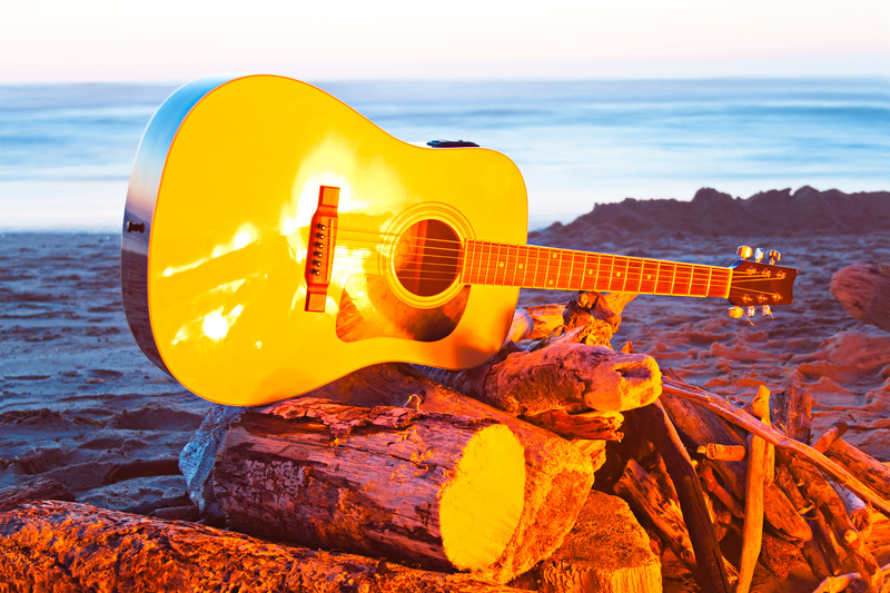 Image of a yellow guitar on a beach bonfire.